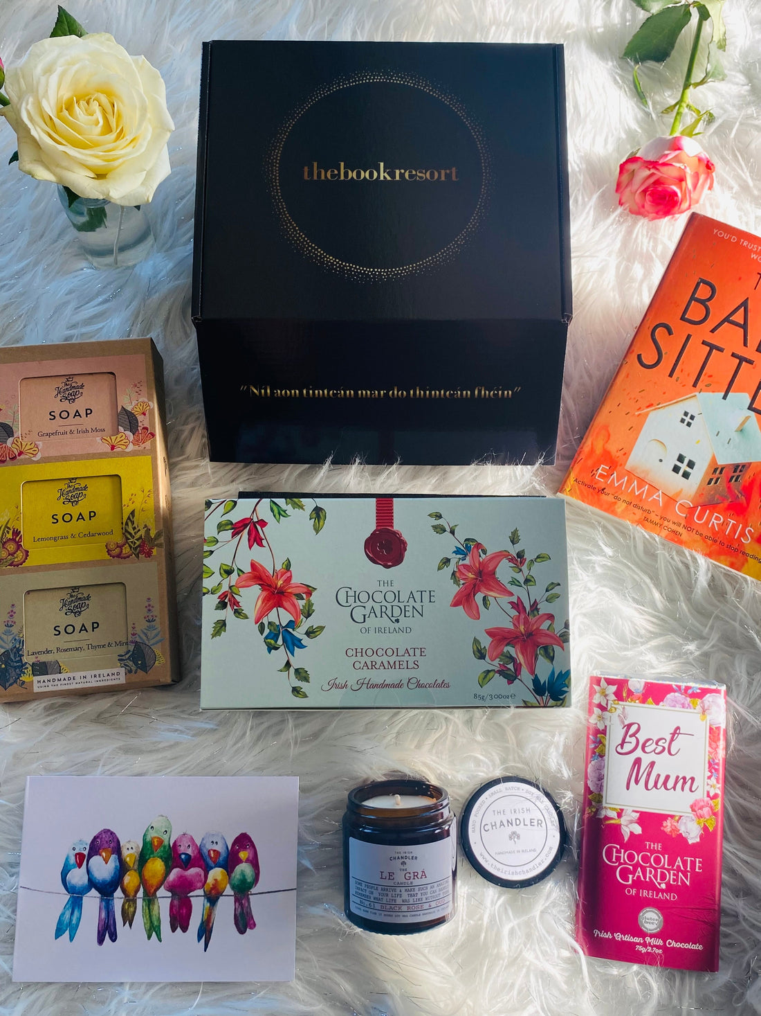 Top-down view of a luxury hand-packed Mother's Day gift hamper from The Book Resort Ireland, featuring a new bestseller book, a bar of artisan Irish chocolate, and a luxury scented candle in a signature glossy box.